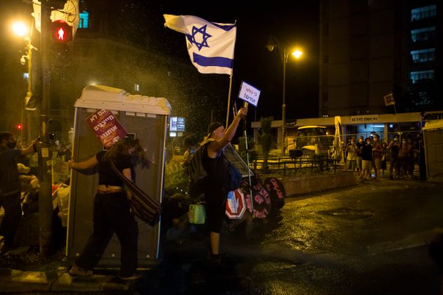 25일 예루살렘에서 집회 참가자가 물대포를 쏘는 경찰들을 향해 깃발과 구호를 적은 카드를 흔들고 있다.