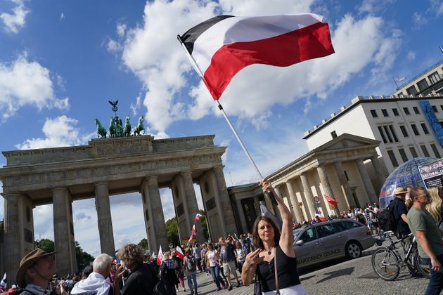 정부의 코로나19 방역 지침 항의시위에서 한 여성이 독일제국 깃발을 든 채 독일의 유명 음모론자 아틸라 힐트만(Attila Hildmann)을 지지하는 손가락 제스처를 취하고 있다. 베를린, 독일. 2020년 8월29일.