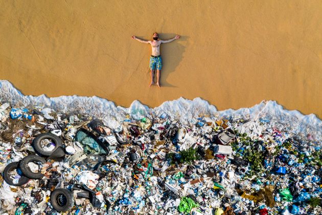 한 남성이 쓰레기로 뒤덮인 해변가에 누워 있다.