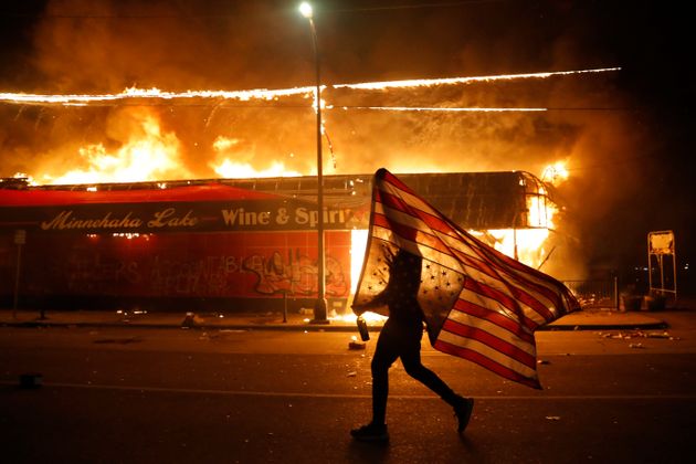 백인 경찰관의 '목조르기' 체포로 흑인 조지 플로이드가 사망한 사건에 항의하는 시위에서 한 시위자가 미국 국기를 거꾸로 든 채 불타는 상점 앞을 지나고 있다. 미니애폴리스, 미네소타주, 미국. 2020년 5월28일.