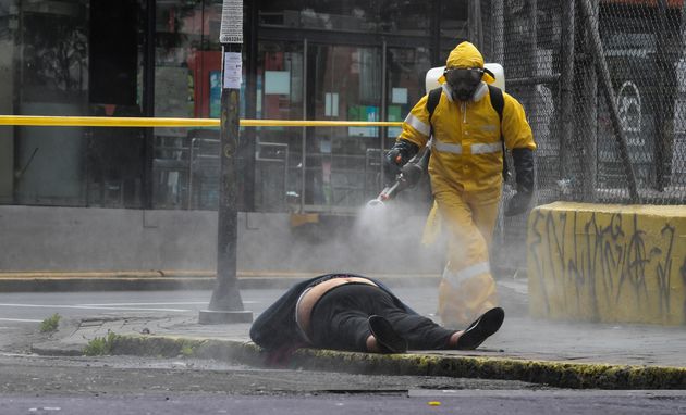 에콰도르 키토시 보건당국자가 길거리에 쓰러진 채 사망한 한 여성의 시신을 소독하고 있다. 당국자들이 현장에서 고인에 대한 코로나19 검사를 실시한 결과는 음성이었다. 2020년 5월14일.