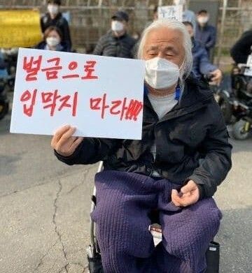 18일 박경석 전국장애인야학협의회 이사장이 “벌금으로 입 막지 마라!!!”고 쓴 손팻말을 들고 있다.