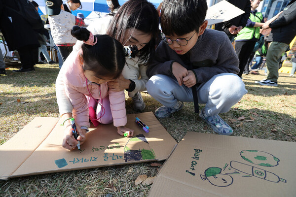 유엔 플라스틱 협약 제5차 정부 간 협상위원회 회의를 이틀 앞둔 23일 오후 부산 해운대구 올림픽공원 일대에서 열린 ‘1123 부산 플라스틱 행진’ 참가자가 엄마와 오빠 도움을 받아 손팻말을 만들고 있다. ⓒ한겨레